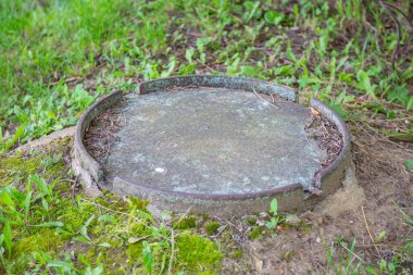 Yeşillik çimenlerin arasında eski, yuvarlak bir rögar.