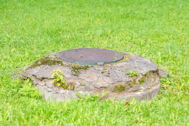Yeşillik çimenlerin arasında eski, yuvarlak bir rögar.
