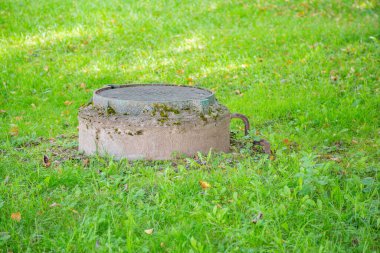 Yeşillik çimenlerin arasında eski, yuvarlak bir rögar.