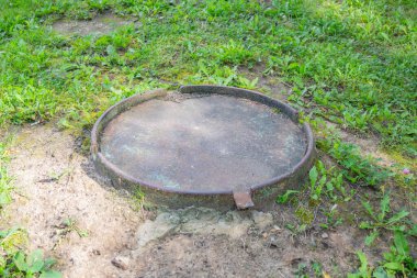 Yeşillik çimenlerin arasında eski, yuvarlak bir rögar.