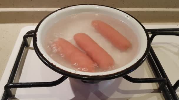 3つの調理されていないソーセージは ガスストーブの上で水で煮込まれます — ストック動画