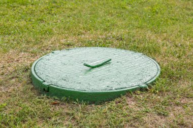 Yeşillik çimenlerin arasında eski, yuvarlak bir rögar.