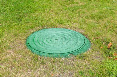 Yeşillik çimenlerin arasında eski, yuvarlak bir rögar.