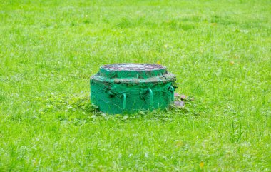 Yeşillik çimenlerin arasında eski, yuvarlak bir rögar.