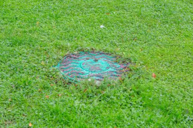 Yeşillik çimenlerin arasında eski, yuvarlak bir rögar.