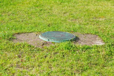 Yeşillik çimenlerin arasında eski, yuvarlak bir rögar.