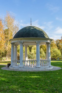 Yeşil bir parkta ziyaretçilerin dinlenmesi ve dinlenmesi için beyaz taştan yapılmış bir çardak.