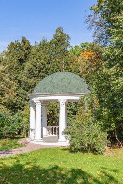 Yeşil bir parkta ziyaretçilerin dinlenmesi ve dinlenmesi için beyaz taştan yapılmış bir çardak.