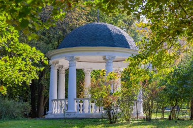 Yeşil bir parkta ziyaretçilerin dinlenmesi ve dinlenmesi için beyaz taştan yapılmış bir çardak.