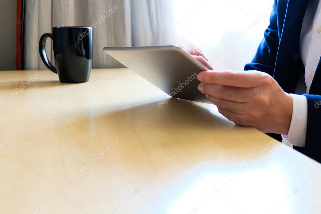 Man business person with suit using tablet device reading news or check for financial stock exchange information while drinking coffee in the morning at the cafe or office. with copy space for text