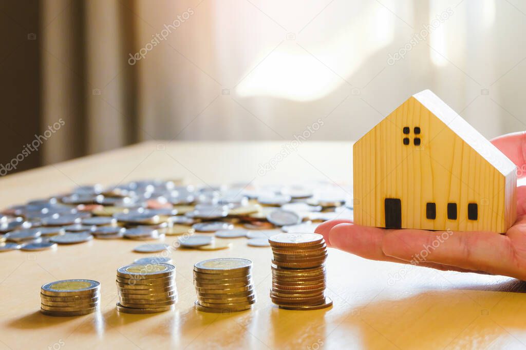 Men hand hold, giving wood house beside increasing money, coin stack on wood table. Saving plan to buy property, house. Personal financial concept for own a house. with copy space for text