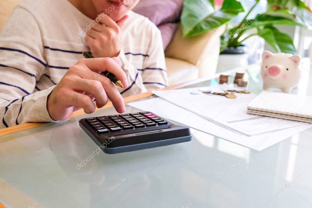 Selective focus of Asian men hand while calculate and think about personal saving with document and piggy bank at the background.