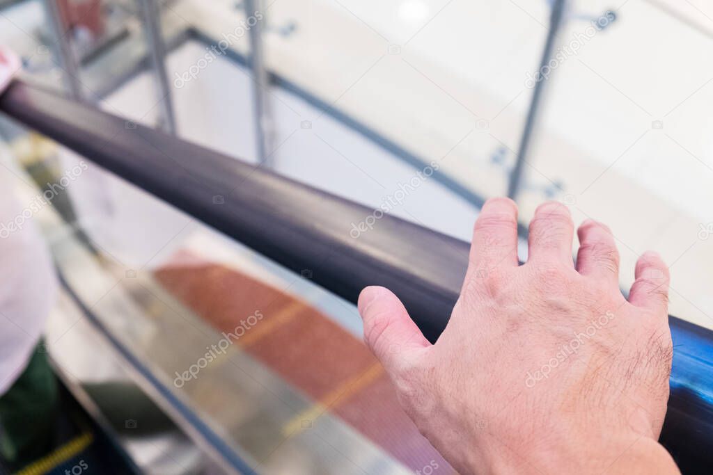 Selective focus at men hand reaching to grab handrail of escalator. Inside department store, public area.  Avoid to touch any surface to prevent coronavirus  infect.