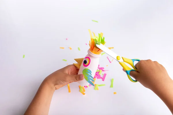 Barn gör ett hantverk av papper och återvunnen yoghurt flaska, DIY Papperspapper papegoja. Dagis och skolverksamhet — Stockfoto