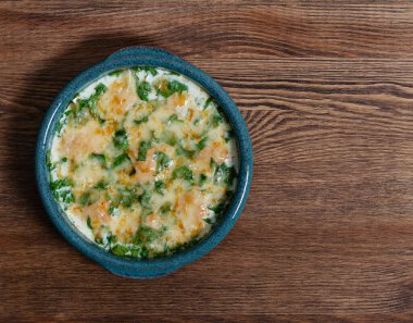 Fırında pirzola, ıspanak soslu, ahşap bir masada peynirli fırın kabında.