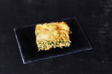 Siyah bir arka planda bir lazanya parçası.