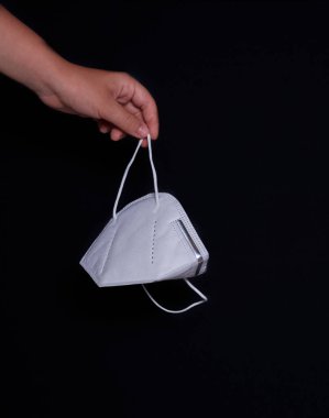 Koruyucu maskeli bir kadın eli, siyah arka plan, Covid-19.