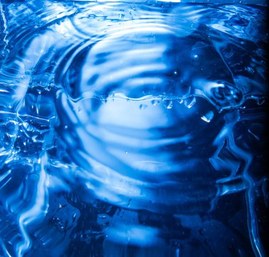 Su yüzeyinin 470 'i dalga halkalarını ve dalga dokusunu gösteriyor. Mavi ışık soyut yansımalar yaratır. Görüntü akışkan hareketi, yüzey gerilimini ve çarpışmadan dalga yayılmasını yakalar.