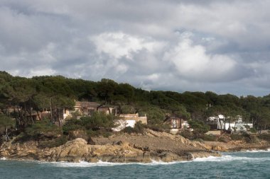 İspanya 'nın Mallorca eyaletinin Cala Ratjada kıyısındaki kayalıklarda bulunan ormandaki evler. Akdeniz 'in fırtınalı dalgaları. Güneşli bir gün.