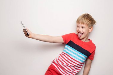Küçük çocuk beyaz arka planda izole cep telefonu ile selfie çekiyor. Stüdyo portresi
