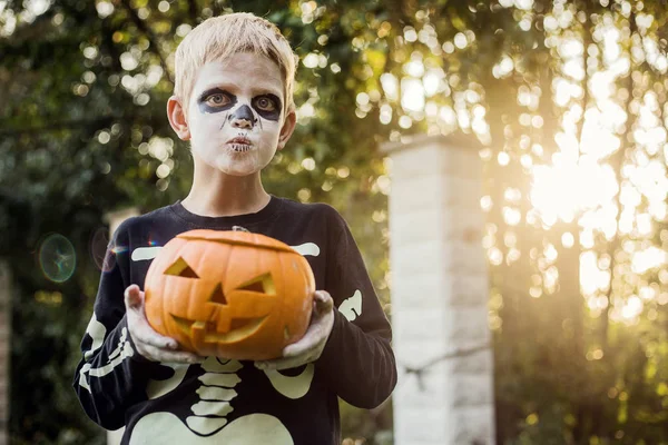 ジャックOランタンを保持スケルトン衣装を持つ幸せな若いブロンドの髪の少年 ハロウィーン お菓子をくれないといたずらするよ 屋外の肖像画 ストック画像