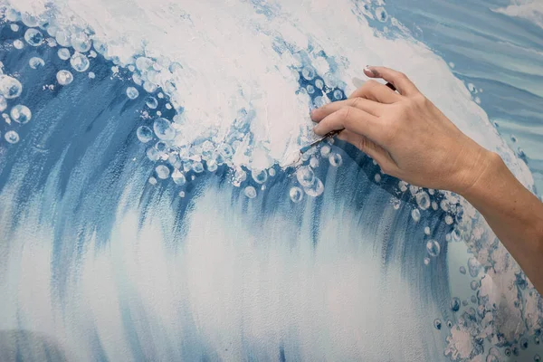 Woman artist paints mural in a living room. The theme of the picture is the sea. Hand close up.