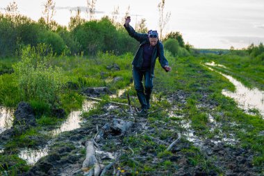 Suddenly an obstacle. A lot of dirt on a forest road after rain. Hiker woman overcomes the barrier. Yelnia Bog, Belarus clipart