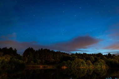 Akşam manzarası: Bulutlarda yıldızlı bir gökyüzü ve güneş battıktan hemen sonra bir orman gölü üzerinde Neowise kuyruklu yıldızı. Uzun gece manzarası. 