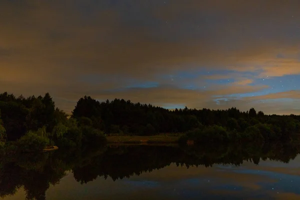 Evening landscape: a starry sky in the clouds and a comet Neowise over a forest lake just after sunset. Bright sunset sky with first stars. Long exposure night landscape.