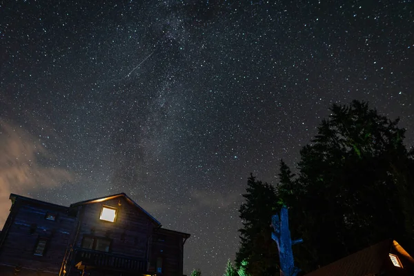 Gece dramatik manzarası. Gökyüzü ve Samanyolu 'nun arka planında kır evi ve ağaçlar var.