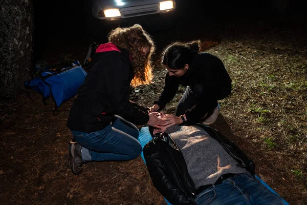 Dwie Kobiety Pomagają Mężczyźnie Leżącemu Ziemi Nocna Scena Reflektorach Samochodu — Zdjęcie stockowe