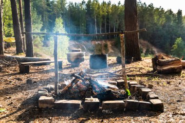 Yemekler bir kamp alanında iki tavada pişiriliyor. Kamp ateşi yakma aletleri. Güzel bir yerde açık hava pikniği..