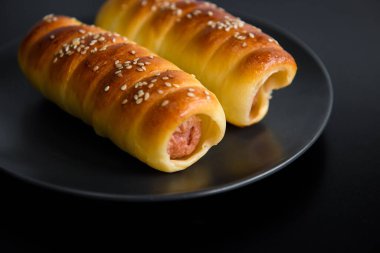 Hamurda sosis pişmiş. Fast food fotoğraf konusu siyah arka planda..
