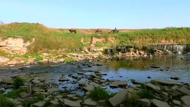 Jinetes a caballo por las pintorescas colinas cerca de la cascada. — Vídeo de stock