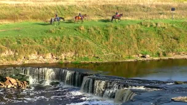 Всадники на лошадях по живописным холмам возле водопада. — стоковое видео