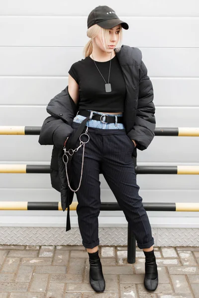 时尚时尚的模特女士穿着时尚的黑色冬季夹克 时尚的帽子 在一个金属墙上摆着时髦的牛仔裤裤 — 图库照片
