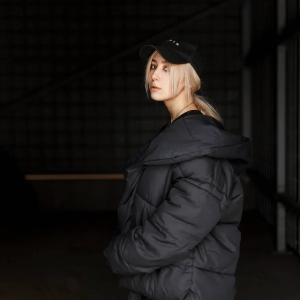 时尚美丽的年轻女子模特在黑色时尚的冬季夹克黑色时尚帽在黑暗背景 — 图库照片