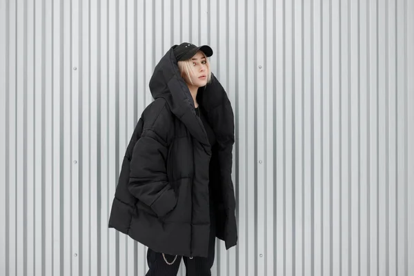 时尚美丽时尚的年轻模特女孩在黑色的冬季夹克与时尚黑色帽附近的金属墙 — 图库照片