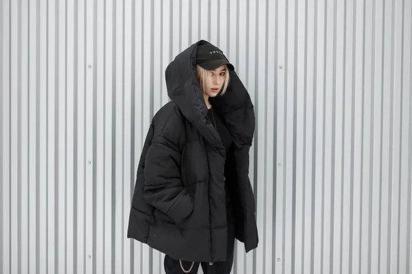 黒のおしゃれな帽子とモダンな金属壁の近く黒いスタイリッシュな冬ジャケットのファッション モデル女性 — ストック写真