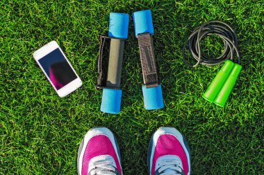 Spor kavram. Kadın bacakları dambıl, telefon ve atlama ipi ile yeşil çimenlerin üzerinde ayakkabı ile. Aktif yaşam tarzı