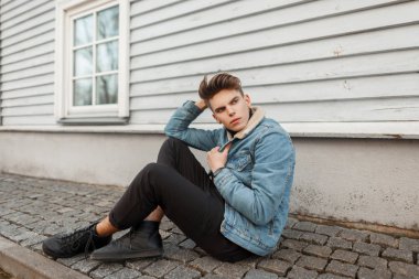 Moda kot vintage giysileri evin yanında bir ahşap duvarının yakınında oturan bir saç kesimi ile şık genç adam