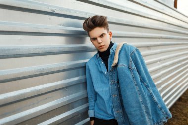 Bir saç modeli şık denim ceket ve kot gömlek şık moda adamla kalın metal duvar yakınında sokakta