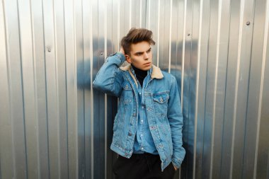Vintage moda denim giysiler bir metal duvar yakınındaki bir saç modeli ile yakışıklı genç