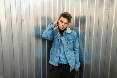Yakışıklı genç adam dışında bir metal duvarın önünde poz moda denim giysi ve kot gömlek