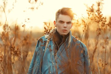 Gün batımında kuru ot bir alana bir kot gömlek moda kot ceket bir saç modeli ile yakışıklı genç
