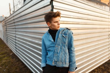 Şık yakışıklı genç bir bahar gününde bir metal duvara yakın poz trendy denim giysileri