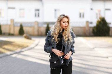 Güzel genç şık kadın modeli ile bir gri şık bir siyah çanta moda ceket, açık havada güneşli bir günde poz