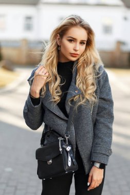 Güneşli bir günde sokakta yürümek moda gri paltolu şık bir çanta ile güzel genç kadın modeli