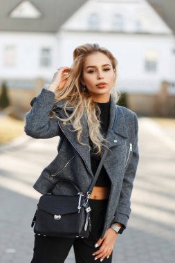 Moda güzel göz alıcı bir kadınla güneşli bir günde dışarıda poz şık bahar gri paltolu bir siyah şık deri çanta
