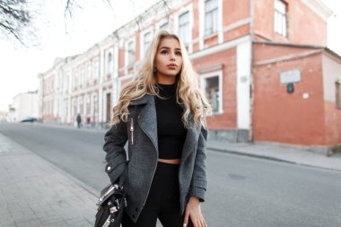 Şehirde bir gri moda ceket, siyah bir çanta moda şık genç kadınla yürüyor 
